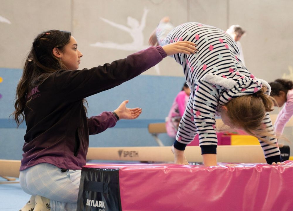 Trainor guiding a young kid on her cartwheel exercise
