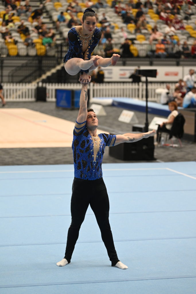 Alex holding Mia in one arm press above his head at acrobatics competition