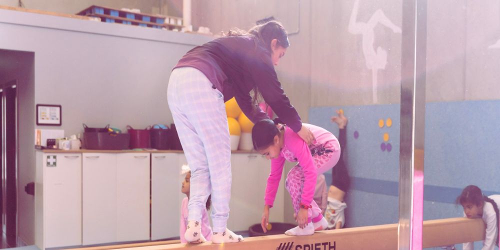 Child and coach doing a gymnastic balance beam training - Skylark Sports