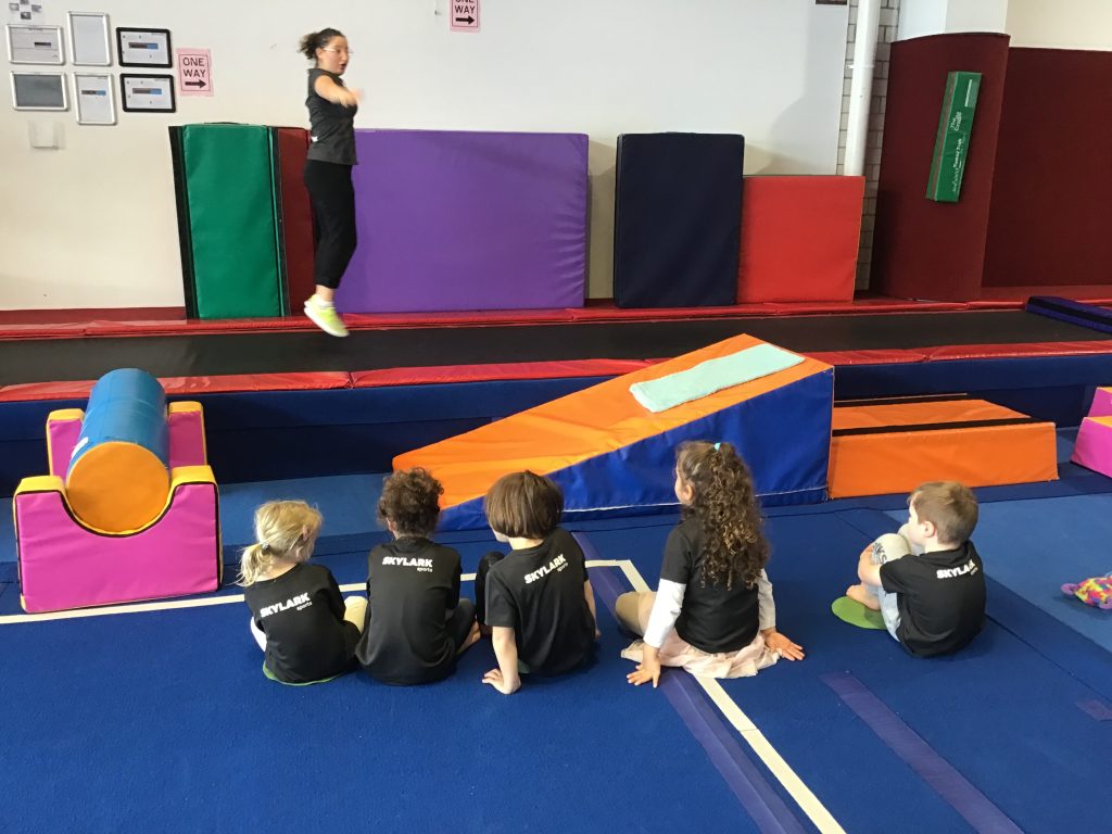 Kindergym class watching coach give instructions for trampoline activity