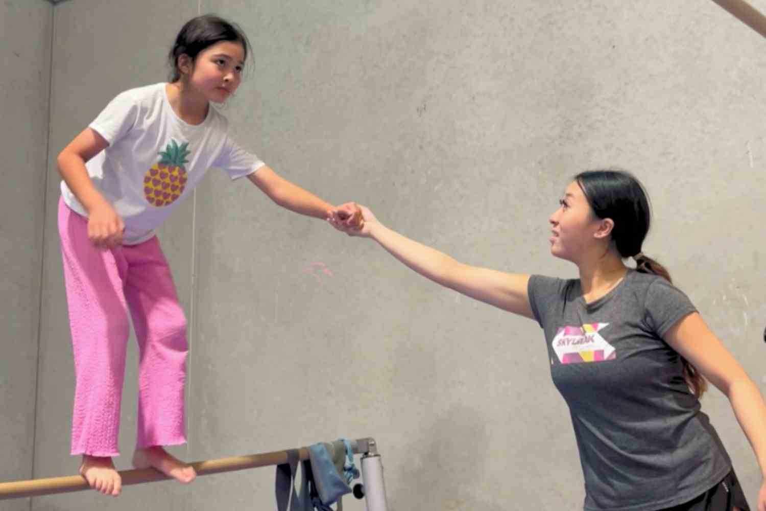 Coach guiding her trainee take a leap from a wooden pole bar.