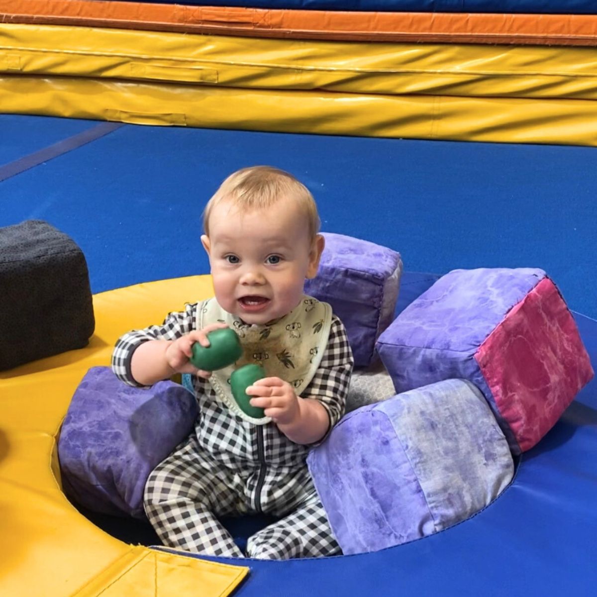 Baby holding toy while sitting on a kindergym floor